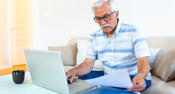 Focused greyhaired elderly man sit couch reading bank notifications calculating domestic expenditures concentrated modern mature male consider financial paperwork pay bills laptop online web